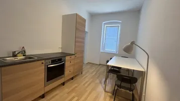Funktionale Küchenzeile mit Holzelementen, integriertem Backofen und Essbereich am Fenster.
