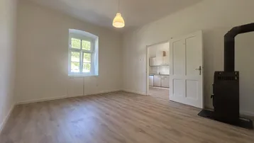 Geräumiger, heller Raum mit Laminatboden, Kaminofen und Zugang zu einem weiteren Zimmer.