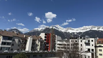 Panoramablick über städtische Dächer auf schneebedeckte Berge unter einem klaren, blauen Himmel.