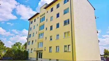 Mehrstöckiges Wohngebäude mit gelber Fassade und vielen Fenstern unter blauem Himmel.