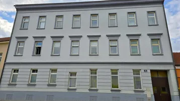 Klassische Fassade eines Mehrfamilienhauses mit zahlreichen Fenstern und schlichten Verzierungen.