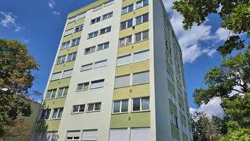 Mehrstöckiges Wohngebäude mit hellgrüner und weißer Fassade unter blauem Himmel.