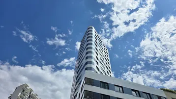 Modernes Hochhaus mit markanter Fassade und vielen Fenstern unter blauem Himmel.