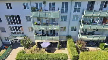 Ansicht eines Mehrfamilienhauses mit Balkonen und einem gepflegten Gartenbereich im Vordergrund.