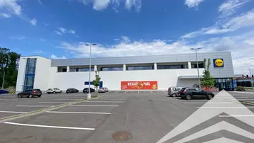 Außenansicht eines modernen Geschäftsgebäudes mit großem Parkplatz unter blauem Himmel.