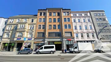 Mehrstöckiges Gebäude mit Geschäften im Erdgeschoss und Wohnungen darüber, an einer belebten Straße gelegen.