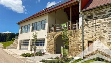 Modernes Gebäude mit traditionellen Steinelementen, Garagen und Solaranlage unter blauem Himmel.