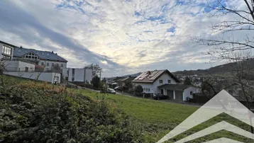 Blick auf die umliegende Wohnsiedlung mit Häusern und grünen Hügeln unter bewölktem Himmel.