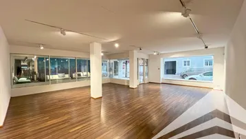 Geräumiger, leerer Geschäftsraum mit großen Schaufenstern und Holzboden, ideal für Laden oder Büro.