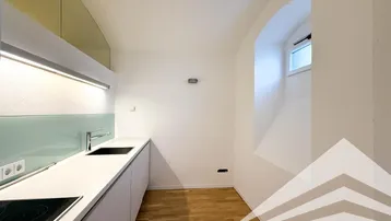 Moderne Küchenzeile mit weißen Schränken, Induktionskochfeld und kleinem Bogenfenster.