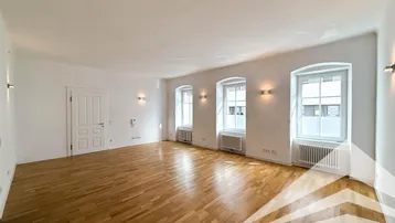 Helles, leeres Zimmer mit Holzboden und drei hohen Fenstern, ideal für einen Wohnbereich.