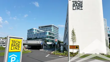 Moderne Bürogebäude mit Glasfassaden und Beschilderung für Tech Base Linz und Tiefgaragenzufahrt.