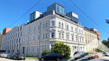 Historisches Gebäude mit modernem Dachausbau und umliegenden Parkplätzen unter blauem Himmel.