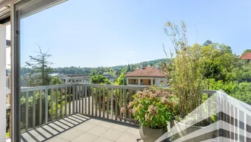 Geräumiger Balkon mit Fliesenboden, Pflanzen und weitem Blick ins Grüne.