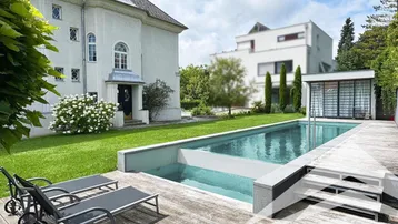 Großer Außenbereich mit Swimmingpool, Holzdeck und Liegestühlen vor der Villa.