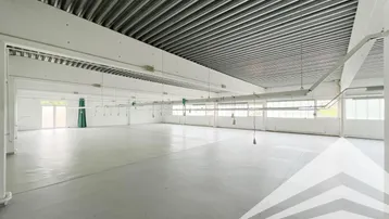 Große, leere Industriehalle mit hohen Decken, Wellblechdach und vielen Fenstern für Tageslicht.