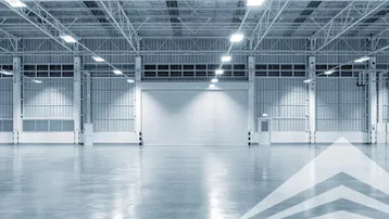 Große, leere Lagerhalle mit hohen Decken, glattem Betonboden und einem großen Rolltor.