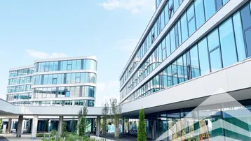 Moderne Bürogebäude mit geschwungenen Glasfassaden und gepflegten Außenanlagen unter blauem Himmel.
