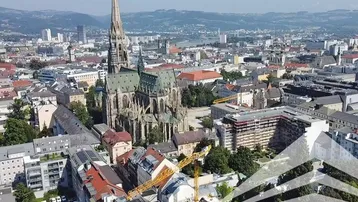 Panoramablick über eine Stadt mit historischer Kathedrale und Bergen im Hintergrund unter blauem Himmel.