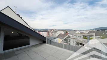 Geräumige Dachterrasse mit Fliesenboden und weitem Blick über die Stadt und die umliegende Landschaft.