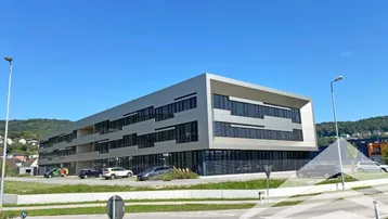 Modernes Geschäftsgebäude mit klarer Architektur und Parkplätzen unter blauem Himmel.