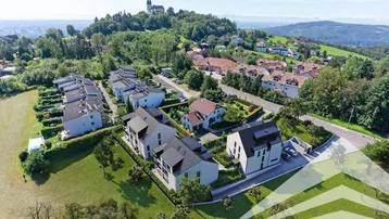 Luftaufnahme einer modernen Wohnsiedlung mit Neubauten und einer Kirche auf dem Hügel im Hintergrund.