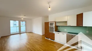 Heller offener Wohnbereich mit integrierter Küche, Parkettboden und Zugang zum Balkon.
