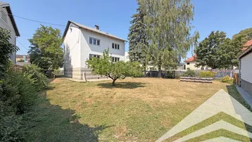 Großer Gartenbereich mit Rasenfläche und einem Baum vor dem Wohnhaus unter blauem Himmel.