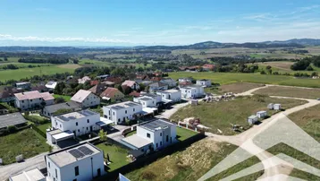 Luftaufnahme einer modernen Wohnsiedlung mit Neubauten und unbebauten Grundstücken in ländlicher Umgebung.