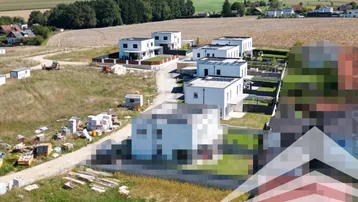 Luftaufnahme einer Siedlung moderner Häuser in ländlicher Umgebung mit weiten Feldern und Hügeln.