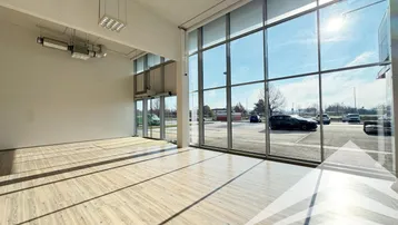 Großer, heller Gewerberaum mit Holzboden und raumhohen Fenstern, die viel Tageslicht hereinlassen.