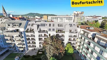 Luftaufnahme eines modernen Wohngebäudes mit Satteldach, Balkonen und begrüntem Innenhof in der Stadt.
