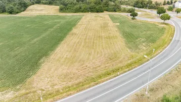 Luftaufnahme eines Grundstücks mit Feldern und einer angrenzenden Straße, umgeben von Bäumen und Häusern in der Ferne.