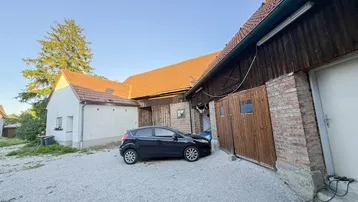 Ländliches Anwesen mit Kiesauffahrt und traditionellen Scheunengebäuden unter klarem Himmel.