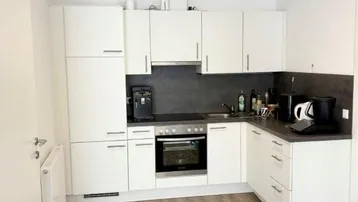 Moderne Einbauküche mit weißen Hochglanzfronten, dunkler Arbeitsplatte und Laminatboden.