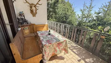 Sonniger Balkon mit traditioneller Sitzbank, Tisch und Bergblick.