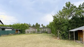 Großer Gartenbereich mit Rasenfläche, umgeben von Hecken und Bäumen, inklusive eines kleinen Holzschuppens.