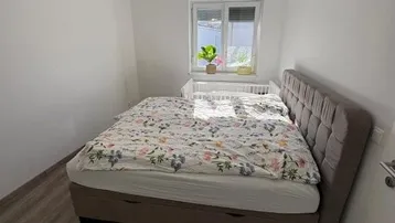 Helles Schlafzimmer mit Doppelbett, Babybett und Laminatboden, ideal für junge Familien.