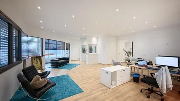 Geräumiges und helles Büro mit modernen Möbeln, großen Fenstern und verschiedenen Arbeitsbereichen.