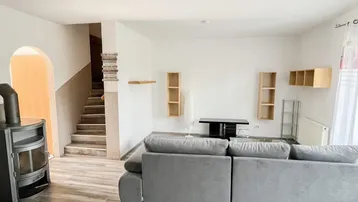 Gemütliches Wohnzimmer mit Holzofen, großem Sofa und Laminatboden, führt zur Treppe.
