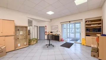 Geräumiger Empfangsbereich mit Fliesenboden, Schränken und automatischen Glastüren zum Eingang.