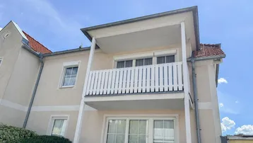 Fassade eines Mehrfamilienhauses mit zwei übereinanderliegenden Balkonen und Satteldach.