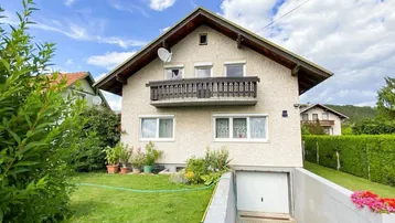 Einfamilienhaus mit gepflegtem Garten, Balkon und integrierter Garage unter blauem Himmel.