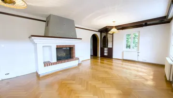 Geräumiges Wohnzimmer mit Fischgrätparkett, Kamin und Holzbalken an der Decke.