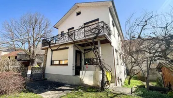 Weißes Einfamilienhaus mit Balkon und Vorgarten unter blauem Himmel.