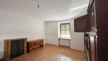 Geräumiges Wohnzimmer mit Holzboden, Kamin und einem Fenster mit Blick ins Grüne.