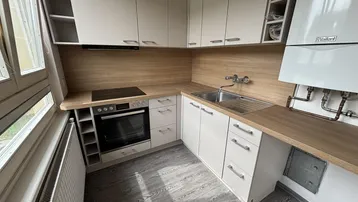 Moderne Küche mit hellen Schränken, Holzarbeitsplatten, integriertem Backofen und Induktionskochfeld.