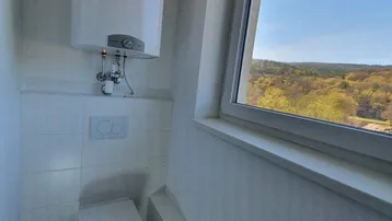 Separates WC mit wandhängender Toilette, Warmwasserboiler und Fenster mit Weitblick.