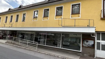 Gelbes Gebäude mit großen Schaufenstern im Erdgeschoss und einer Rollstuhlrampe am Eingang.