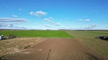 Weitläufige Felder und ein unbebautes Grundstück unter blauem Himmel mit Wolken.